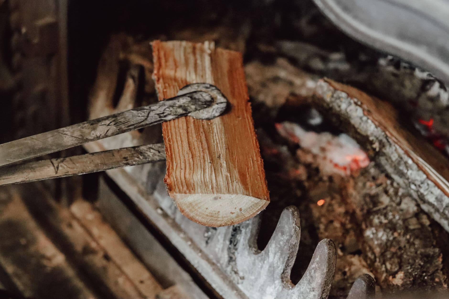 Detailed view of a log being placed into a fireplace with tongs, showcasing warm ambiance.